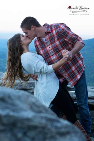 engaged couple kisses at chimney rock overlook at sunset..