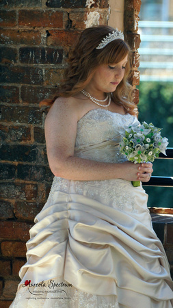 Bride stands by brickwall with handmade bouquet.