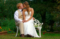 Bride & groom sit on white bench and kiss