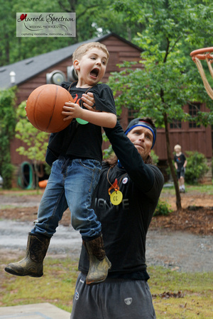 Volunteer lifts heart kid to basketball net at camp luck.
