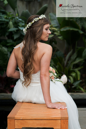 Bride sits on a bench in the orchid conservatory in NC. 